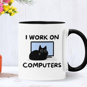 May include: White ceramic mug with a black rim and handle. The mug has a black cat sitting on a laptop with the text "I work on computers" printed on it.
