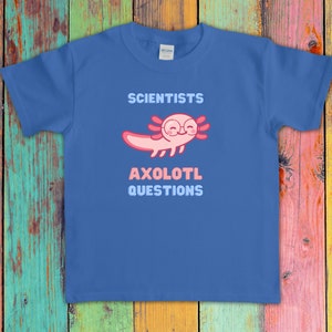 Puede incluir: Una camiseta azul de manga corta con un gr&aacute;fico de un ajolote rosa con gafas redondas. El texto sobre el ajolote dice SCIENTISTS y el texto debajo dice AXOLOTL QUESTIONS en letras de bloque de color azul claro y rosa en el pecho.