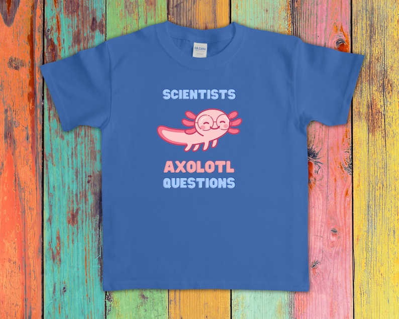 Puede incluir: Una camiseta azul de manga corta con un gr&aacute;fico de un ajolote rosa con gafas redondas. El texto sobre el ajolote dice SCIENTISTS y el texto debajo dice AXOLOTL QUESTIONS en letras de bloque de color azul claro y rosa en el pecho.