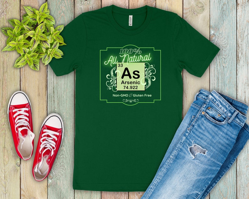 May include: Green t-shirt with a white graphic of a periodic table element. The element is arsenic, with the symbol As, atomic number 33, and atomic weight 74.922. The graphic also includes the text "100% All Natural", "Non-GMO", and "Gluten Free".