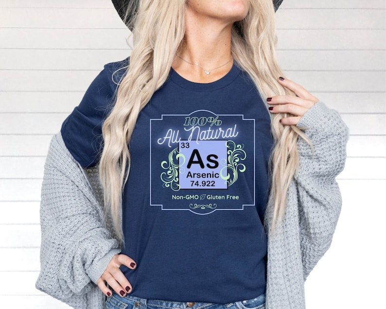 May include: A navy blue t-shirt with a graphic of a periodic table element, arsenic (As), with the text "100% All Natural", "Arsenic", "33", "74.922", "Non-GMO & Gluten Free".