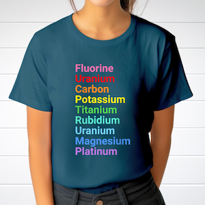 May include: A dark teal short-sleeved t-shirt featuring a vertical list of chemical elements printed in rainbow colors. The text reads: Fluorine, Uranium, Carbon, Potassium, Titanium, Rubidium, Uranium, Magnesium, and Platinum in descending order.