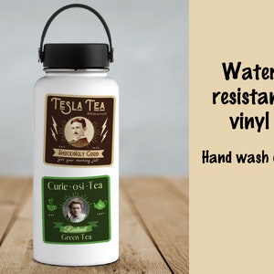 May include: A white water bottle with a black handle and lid. The bottle has two rectangular stickers. The top sticker says "TESLA TEA" with a portrait and lightning bolts. The bottom sticker says "Curie-osi-Tea" with a portrait and tea-related graphics. Text on the right says "Water resistant vinyl" and "Hand wash only."