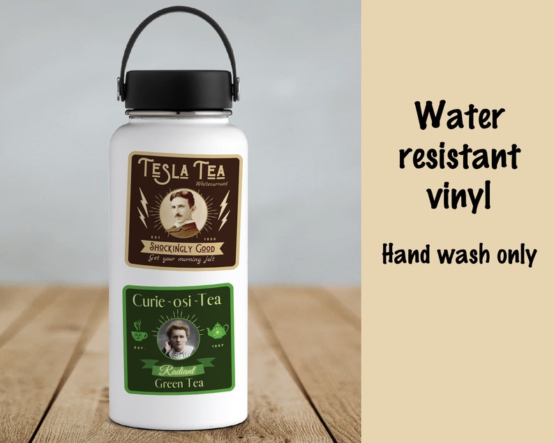 May include: A white water bottle with a black handle and lid. The bottle has two rectangular stickers. The top sticker says "TESLA TEA" with a portrait and lightning bolts. The bottom sticker says "Curie-osi-Tea" with a portrait and tea-related graphics. Text on the right says "Water resistant vinyl" and "Hand wash only."