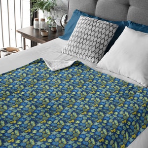 May include: A blue fleece throw blanket with a pattern of yellow and green flowers and leaves. The blanket is folded on a bed with white sheets and pillows.