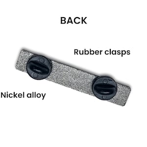 May include: The back of a silver pin with two black rubber clasps. The pin is made of nickel alloy.