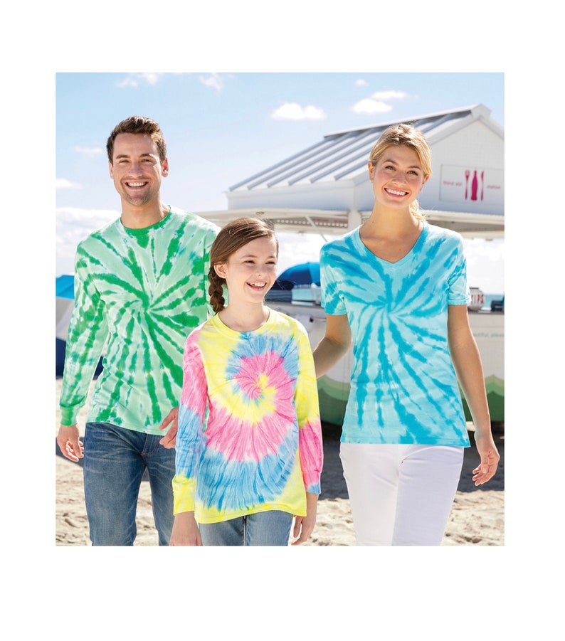 May include: A family of three wearing tie-dye shirts. The father is wearing a green and white tie-dye long-sleeve shirt, the mother is wearing a blue and white tie-dye short-sleeve shirt, and the child is wearing a yellow, pink, and blue tie-dye long-sleeve shirt.