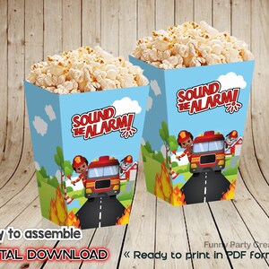Puede incluir: Dos cajas de palomitas de maíz llenas de palomitas de maíz. Las cajas son de color azul claro con nubes blancas y presentan un tema de bombero con un camión de bomberos rojo y el texto "SOUND THE ALARM!". Las cajas están etiquetadas como "Easy to assemble" y "DIGITAL DOWNLOAD".