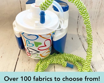 May include: A medical suction machine featuring a white canister with a colorful heart pattern, paired with a long, flexible tube covered in a green and white chevron fabric sleeve. The device includes a blue base and the text Over 100 fabrics to choose from!