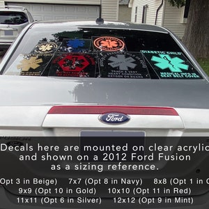 May include: A silver 2012 Ford Fusion with decals on the rear window. The decals are various sizes and colours, including red, blue, green, and beige. The decals feature the Star of Life symbol and text such as "Diabetic Child", "Fragile Child on Board", and "Medical Info in Seat Belt Cover".