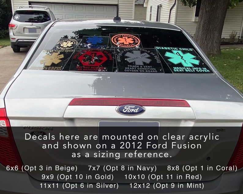 May include: A silver 2012 Ford Fusion with decals on the rear window. The decals are various sizes and colours, including red, blue, green, and beige. The decals feature the Star of Life symbol and text such as "Diabetic Child", "Fragile Child on Board", and "Medical Info in Seat Belt Cover".