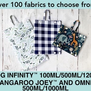 May include: Three rectangular fabric pouches with top handles and white snap closures. One features a green leaf pattern, one has a navy and white buffalo check, and one displays a dark teal print with elephants and giraffes. Text reads: Over 100 fabrics to choose from! MOOG INFINITY 100ML/500ML/1200ML KANGAROO JOEY AND OMNI 500ML/1000ML.