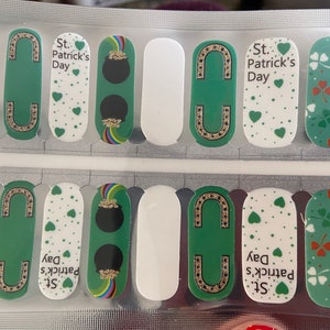 Könnte beinhalten: Nageldesign-Streifen mit St. Patrick's Day-Motiven. Die Streifen haben weiße, grüne und goldene Akzente. Designs umfassen Kleeblätter, Goldtöpfe und den Text "St. Patrick's Day."