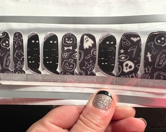 May include: A set of 10 black and white nail wraps with a Halloween theme. The wraps feature images of ghosts, pumpkins, skulls, and other spooky designs.