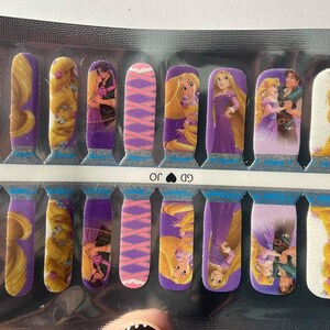 May include: Nail art strips featuring Rapunzel from the animated film Tangled. The strips showcase images of Rapunzel, her long golden hair, and scenes with Flynn Rider. The background colours include purple, pink, and white.