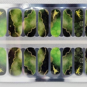 Può includere: Un foglio di wrap per smalto per unghie con un designo a marmo verde e nero con accenti dorati e una silhouette di fata.