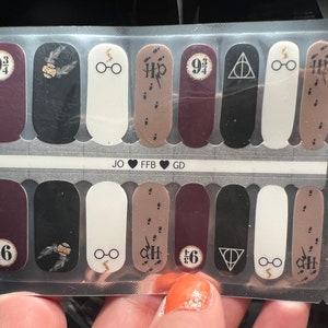 Puede incluir: Una hoja de 12 pegatinas para uñas con temática de Harry Potter. Las pegatinas presentan imágenes del Expreso de Hogwarts, el símbolo de las Reliquias de la Muerte y el número 9 3/4. Las pegatinas son de varios colores, incluyendo marrón, negro, blanco y rojo.