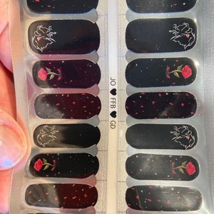Puede incluir: Una lámina de envolturas de uñas negras con una rosa roja y una silueta de un rostro de mujer. La lámina tiene el texto "JO ♥ FB ♥ GD" impreso en ella.