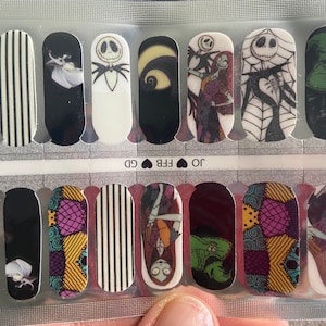 Może przedstawiać: Zestaw 10 naklejek na paznokcie z postaciami z Koszmaru przed Świętami. Naklejki przedstawiają Jacka Skellingtona, Sally i Oogie Boogie. Naklejki są nadrukowane na przezroczystym tle i gotowe do użycia.