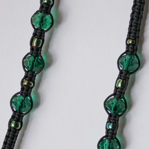 May include: A pair of black cord lanyards with green glass beads and iridescent beads. The lanyards are connected by a silver chain.