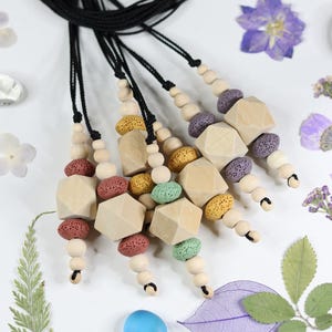 May include: Necklaces with geometric wooden beads and colorful lava rock accents. Each necklace features a black cord and a variety of bead shapes and colors, including red, yellow, green, and purple. The necklaces are displayed on a white surface.