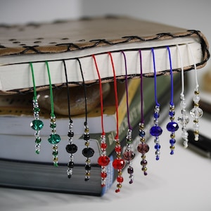 May include: A set of ten beaded bookmarks with different colored strings and crystal beads. The bookmarks are hanging from a leather-bound journal.