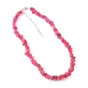 May include: A necklace featuring raw, irregular-shaped ruby gemstones in varying shades of red and pink. The gemstones are strung together, creating a choker-style necklace. The necklace has a silver-colored chain and clasp.