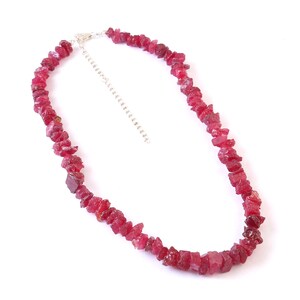 May include: A necklace featuring raw, uncut ruby gemstones in varying sizes. The stones are a deep, rich red color and are strung together with a silver-colored chain and clasp. The necklace is displayed against a white background.