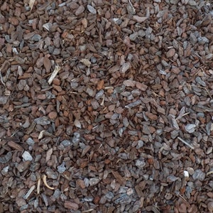 May include: A close-up of a pile of brown and gray wood chips. The chips are small and irregular in shape, and they are scattered randomly across the surface.