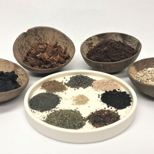 May include: A white plate with nine different types of soil, including coconut husk, charcoal, and potting soil. The soil is arranged in a circle on the plate. The plate is sitting on a white surface.