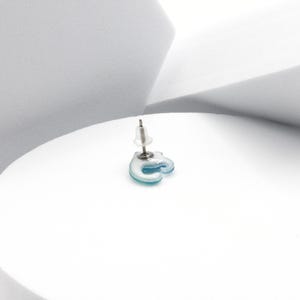 Puede incluir: Un solo pendiente de bot&oacute;n en forma de gato azul y blanco con un poste plateado.