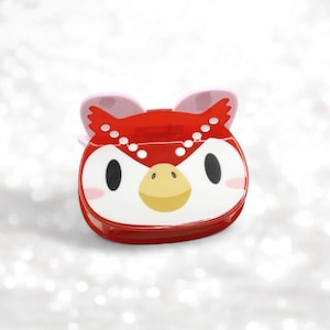 May include: Red and white plastic owl-shaped storage container with a pink beak and ears. The container has a white face with black eyes and a yellow beak.