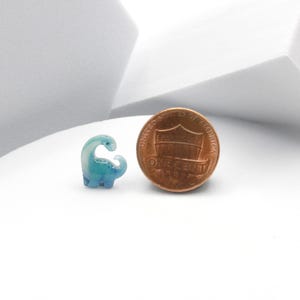 Puede incluir: Una peque&ntilde;a figura de dinosaurio azul y blanco junto a un centavo estadounidense. El dinosaurio es aproximadamente del tama&ntilde;o de un centavo.