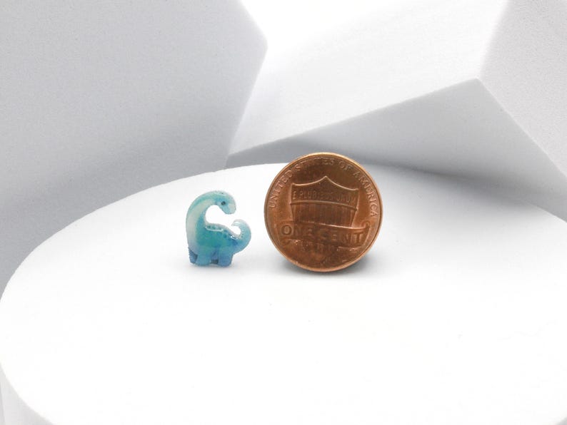 Puede incluir: Una peque&ntilde;a figura de dinosaurio azul y blanco junto a un centavo estadounidense. El dinosaurio es aproximadamente del tama&ntilde;o de un centavo.