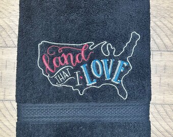 May include: Black bath towel with an embroidered outline of the United States. The text "Land that I Love" is embroidered in red, white, and blue.