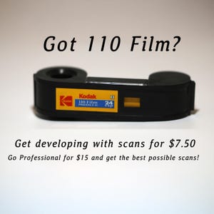 May include: A black Kodak 110 film cartridge with a yellow and blue label. The text "Got 110 Film?" is above the cartridge. The text "Get developing with scans" is below the cartridge.