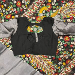 May include: A black blouse with a keyhole back and silver trim. The blouse is on top of a black and white fabric with a peacock design.