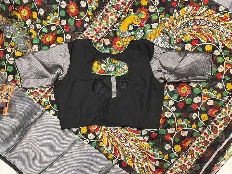 May include: A black blouse with a keyhole back and silver trim. The blouse is on top of a black and white fabric with a peacock design.