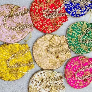 May include: Seven round, embroidered, drawstring bags with pearl and gold chain accents. The bags are in various colours, including pink, red, yellow, green, white, and pink.