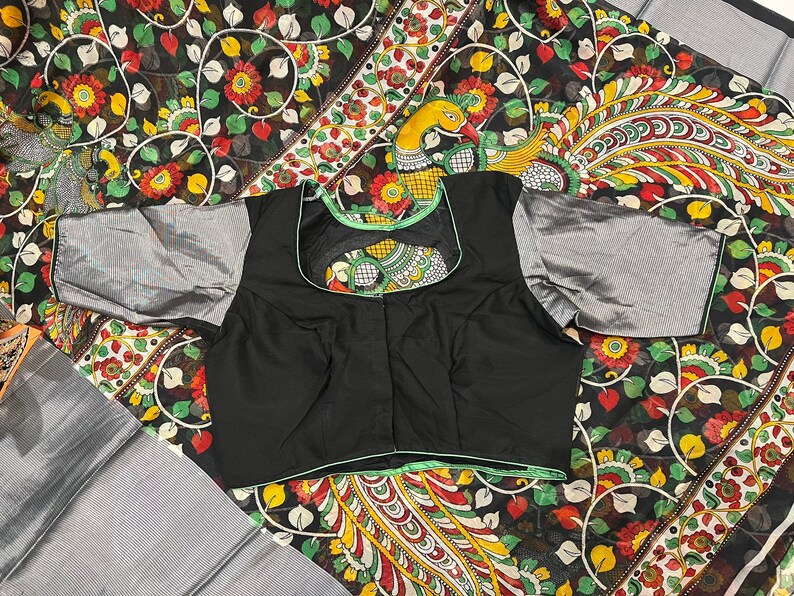 May include: A black blouse with a green trim and a floral pattern on the back. The blouse has a scoop neck and short sleeves.
