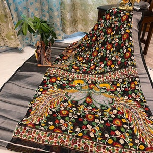 May include: Black and white saree with a floral and peacock design. The saree has a silver border and a red, yellow, and green floral pattern.