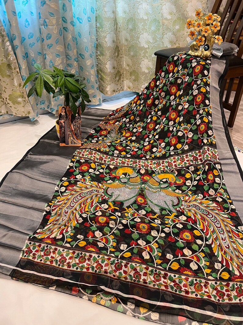 May include: Black and white saree with a floral and peacock design. The saree has a silver border and a red, yellow, and green floral pattern.