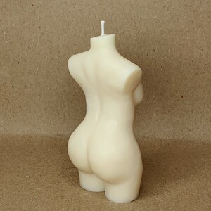 May include: A white candle shaped like a human torso. The candle is made of wax and has a smooth, rounded surface.
