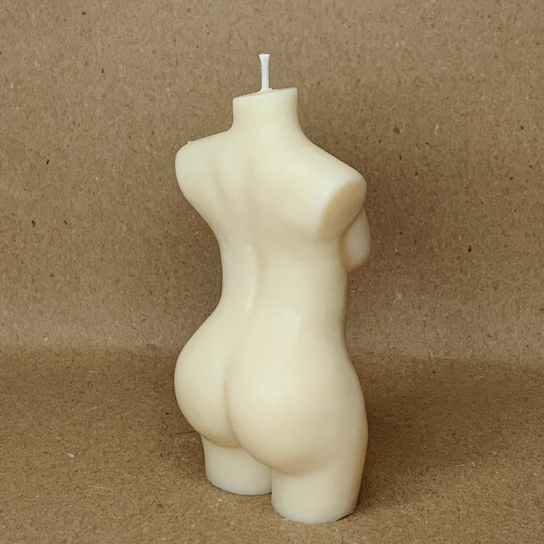 May include: A white candle shaped like a human torso. The candle is made of wax and has a smooth, rounded surface.