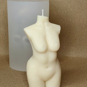 May include: A white candle shaped like a human torso. The candle is smooth and has a rounded shape. It is sitting on a clear silicone mould.