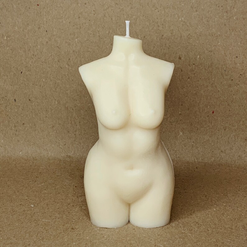 May include: A white candle shaped like a human torso. The candle has a single wick.