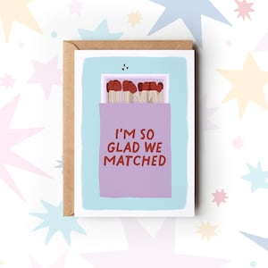 May include: A light blue card with a purple box of matches. The matches have red heads and the box says "I'm so glad we matched".