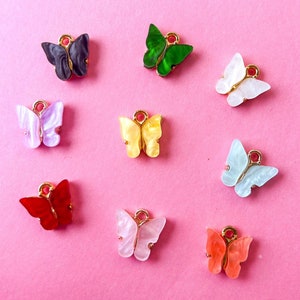 May include: Assortment of ten colorful butterfly charms with gold accents. The butterflies are made of plastic and have a variety of colors, including red, green, blue, yellow, and white.