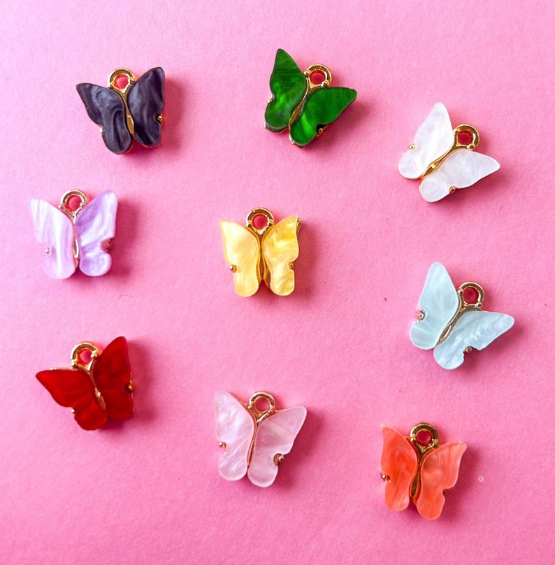 May include: Assortment of ten colorful butterfly charms with gold accents. The butterflies are made of plastic and have a variety of colors, including red, green, blue, yellow, and white.