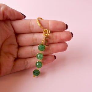 Puede incluir: Llavero dorado con un dije de piedra verde y un dije de letra 'E' dorada. El llavero tiene cuatro piedras verdes.